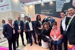 Group of professionals at a trade show booth posing for a photo with banners reading 'SNF' and 'Seven ways to care' in the background.