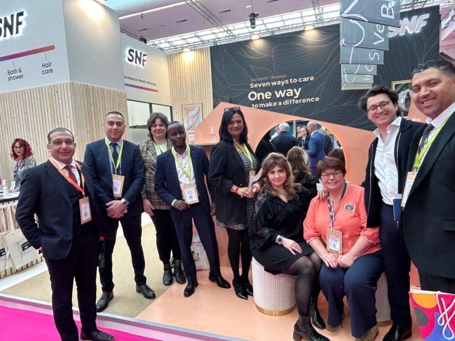 Group of professionals at a trade show booth posing for a photo with banners reading 'SNF' and 'Seven ways to care' in the background.