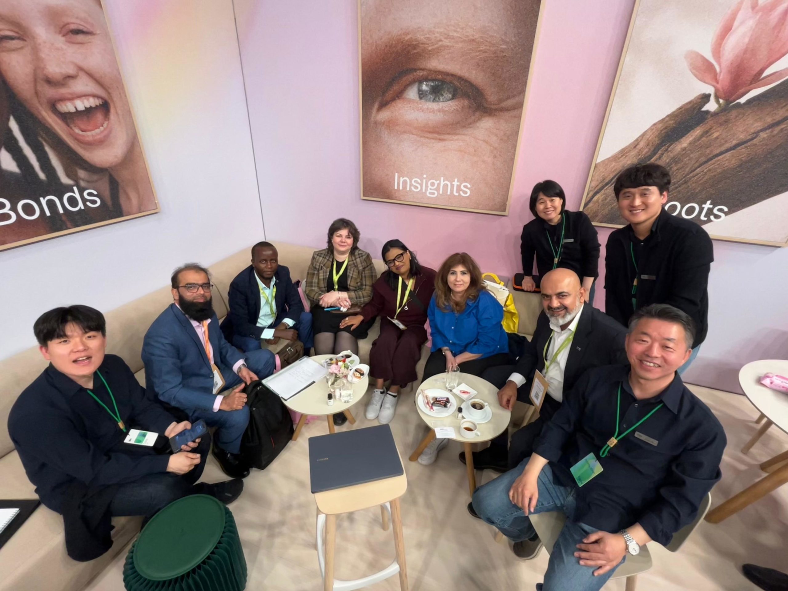 Group of professionals sitting and standing around a small coffee table, smiling for a group photo in a bright, pastel-walled lounge with 'Insights' artwork behind them.