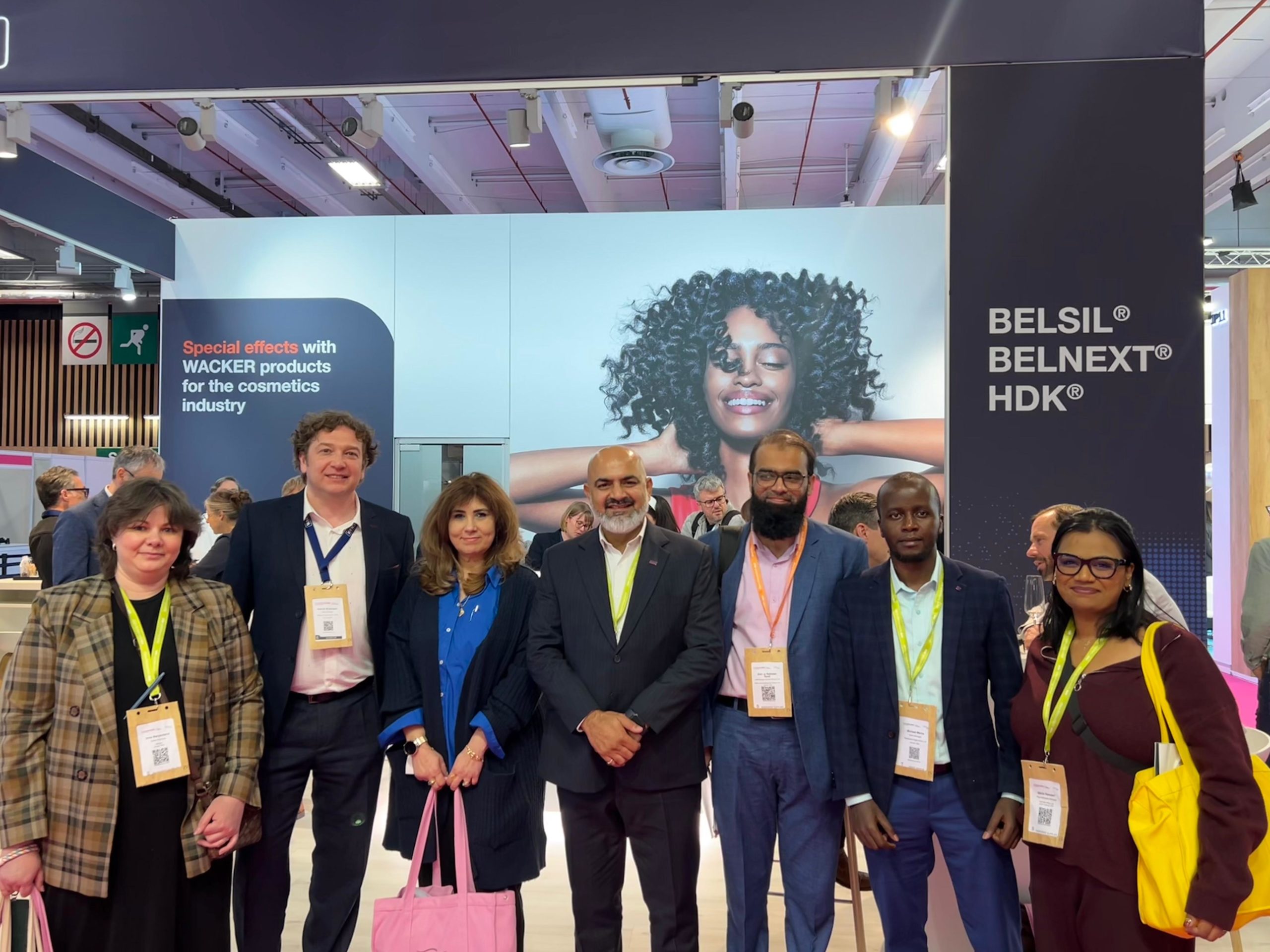 Group of professionals posing for a photo at a trade-show booth with badges and tote bags in hand.