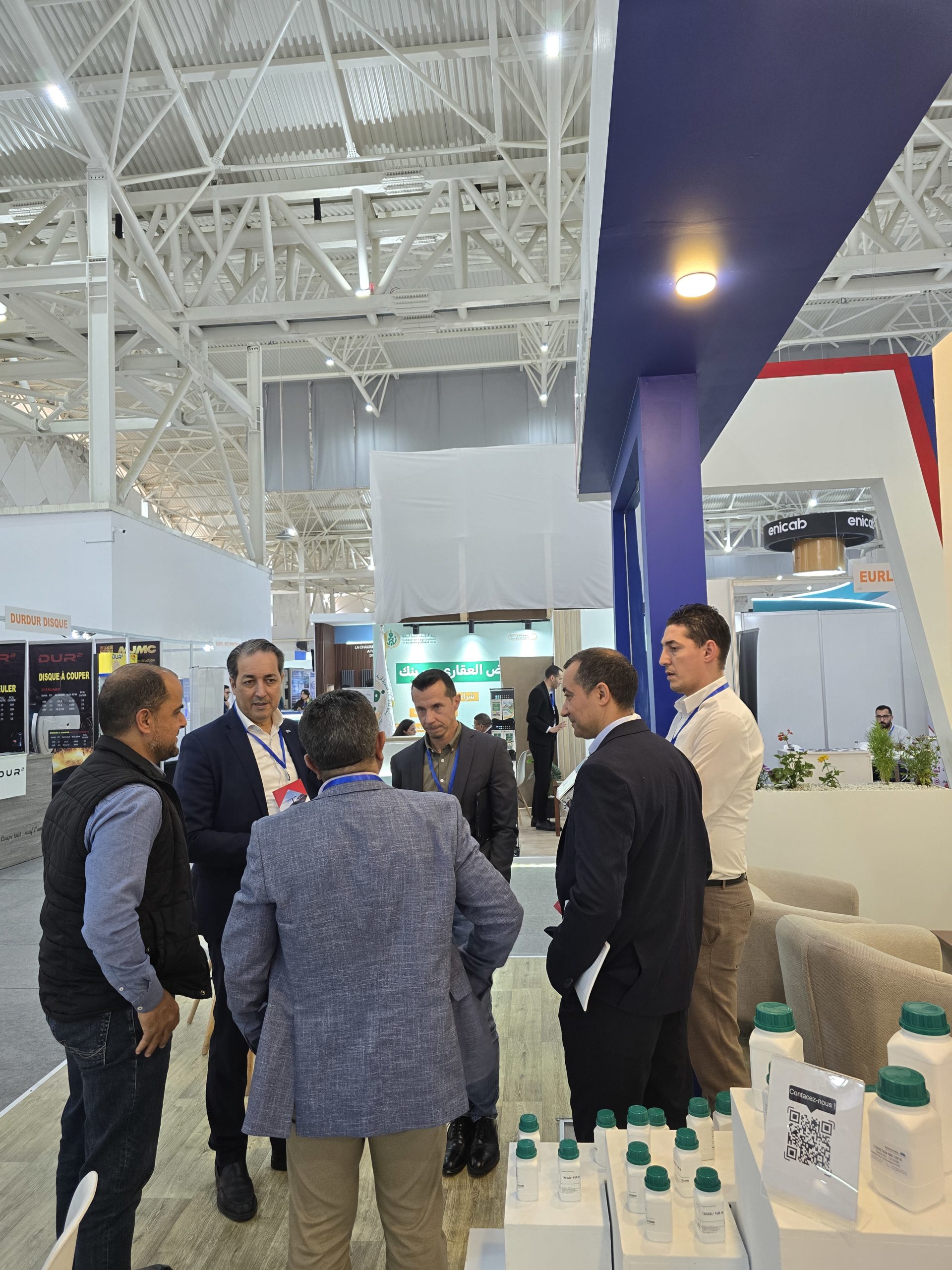 Group of suited men talking at a trade show booth with bottled products on display in the foreground.