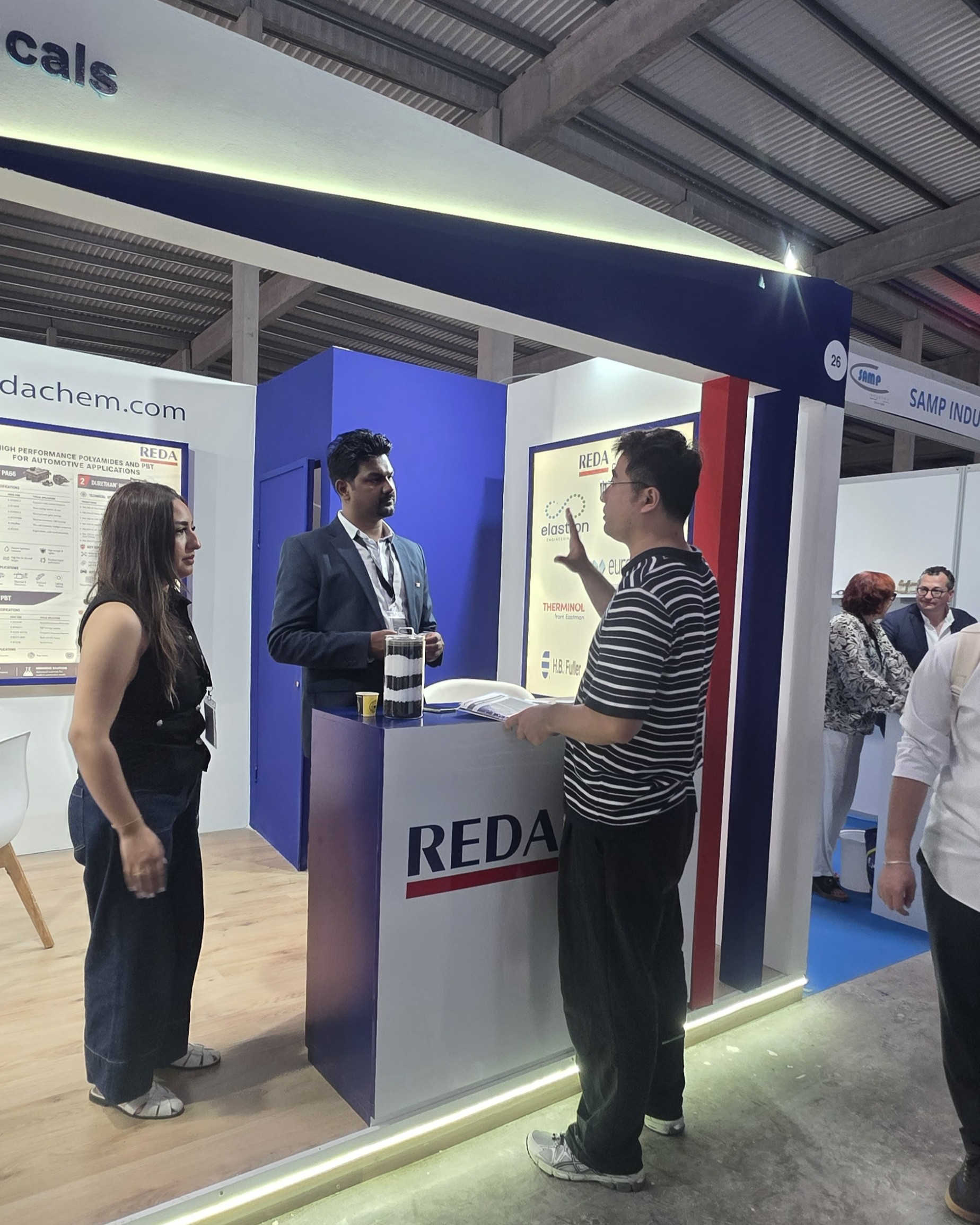 Trade show booth with REDA branding, blue panels, and people standing and talking nearby.