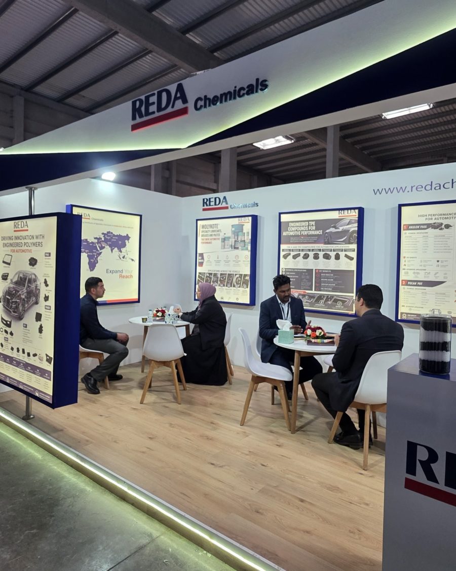 Trade show booth for REDA Chemicals with posters on display and people seated at white tables, discussing products in a modern exhibition hall.