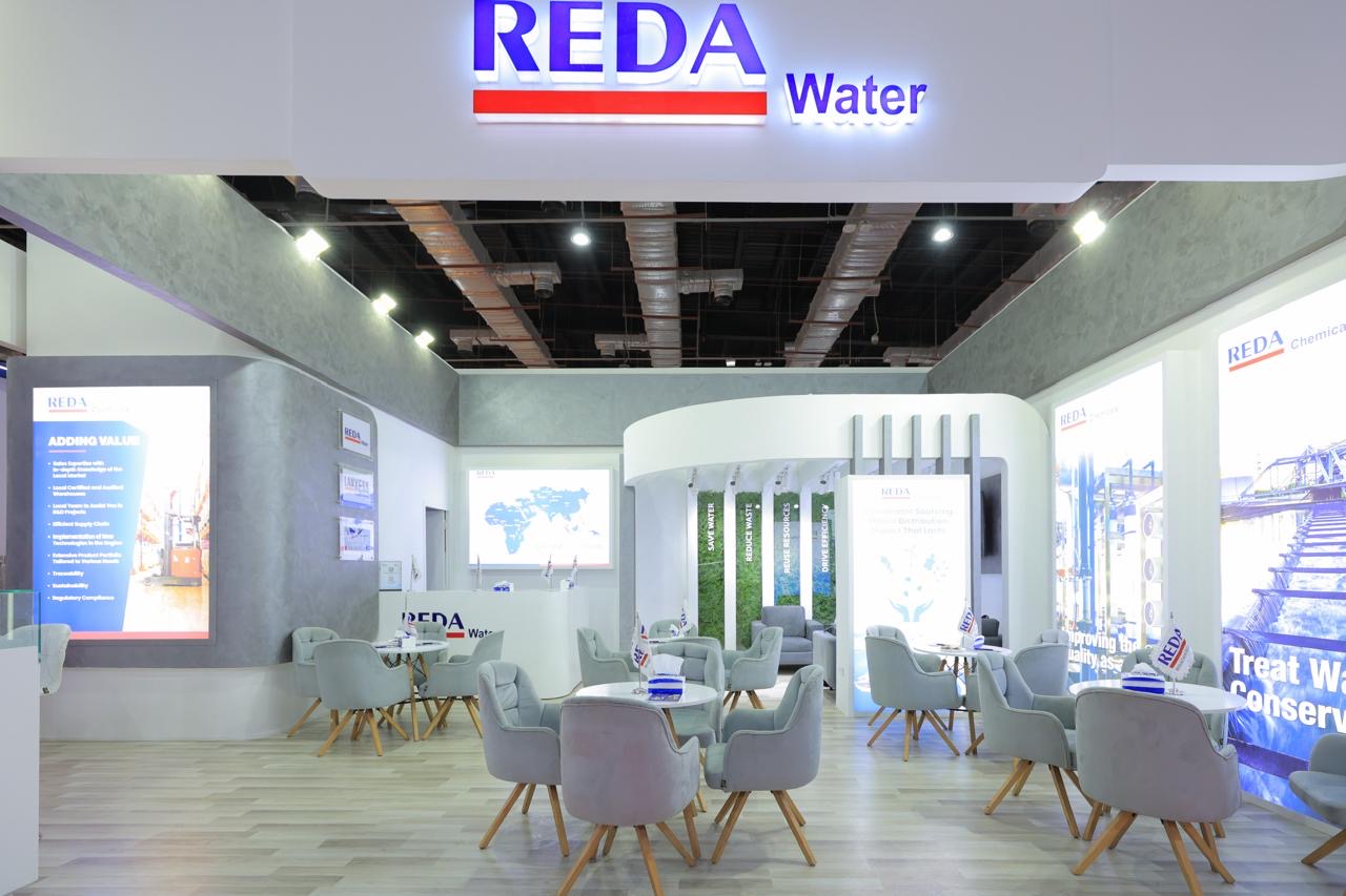 Trade show booth for REDA Water with white/gray decor, round tables and light gray chairs.