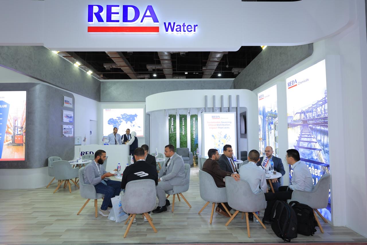 Trade show booth for REDA Water with a seating area where professionals discuss around small tables and chairs.