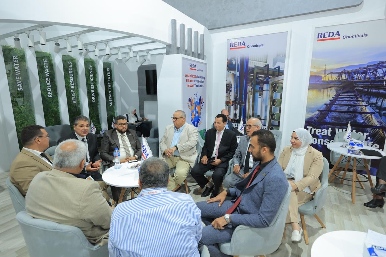 Group of professionals seated in a circle, discussing at a Reda Chemicals expo booth with banners in the background.