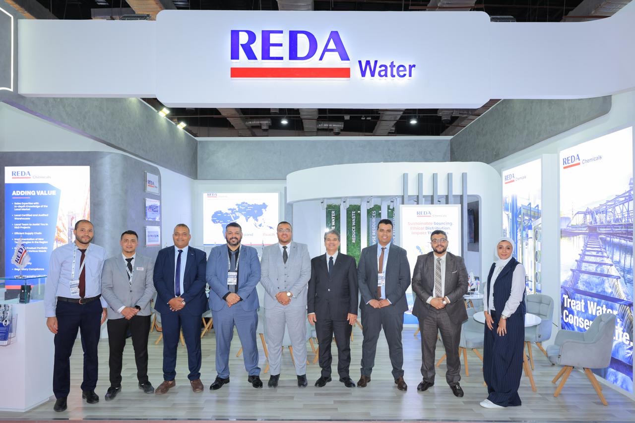 Nine professionals in business attire posing at a REDA Water trade show booth.